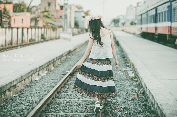 woman wearing white and black dress walking on train rail
