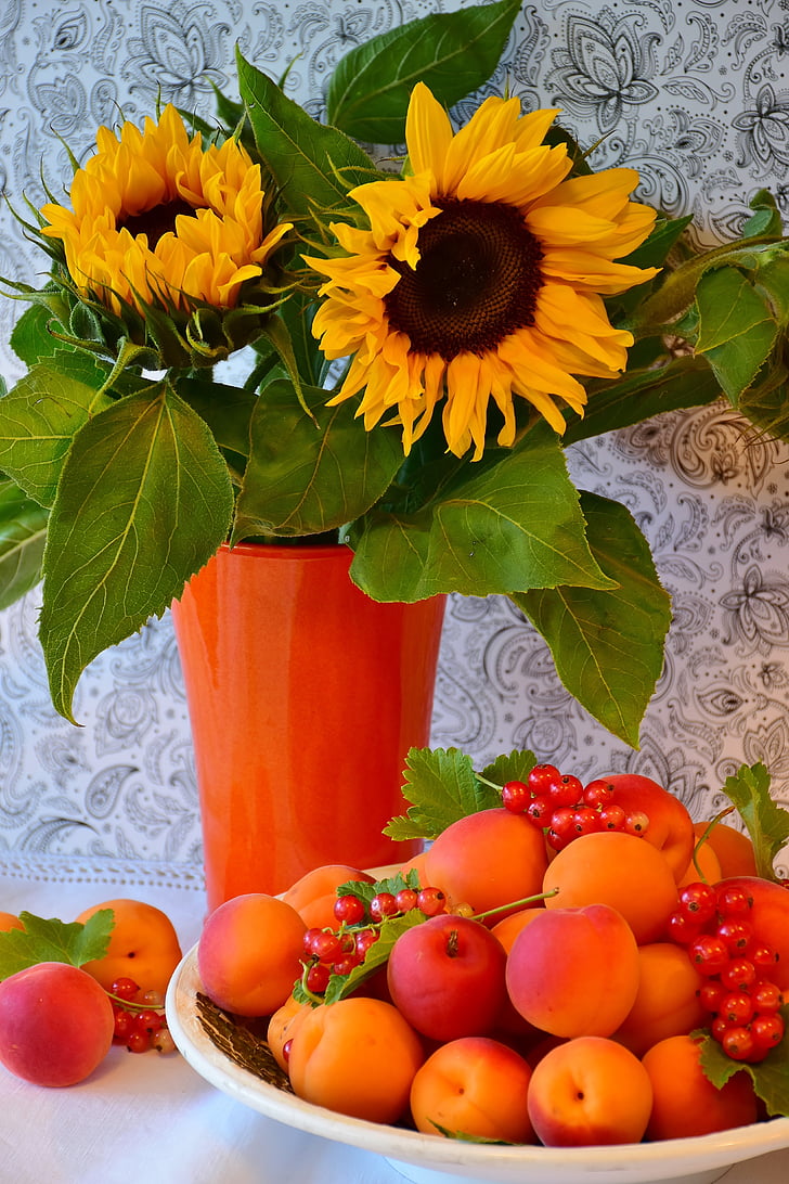 sunflowers with orange vase beside tray of peach and red berries fruits