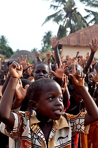 group of children raising hands near trees and building during daytime