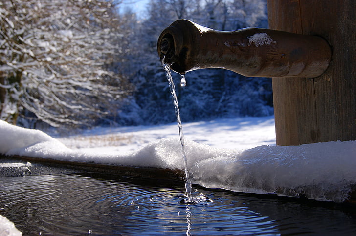 brown bamboo faucet dropping water near trees covered with snow at winter