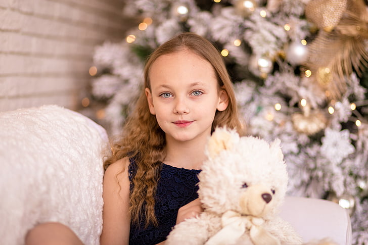girl holding white bear plush toy sitting on sofa