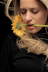 woman wearing black zip-up top biting yellow sunflower