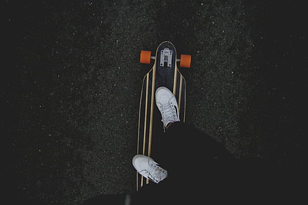 person wearing white sneakers riding black longboard