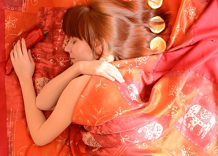 closeup photography of woman sleep on orange and multicolored floral bed comforter