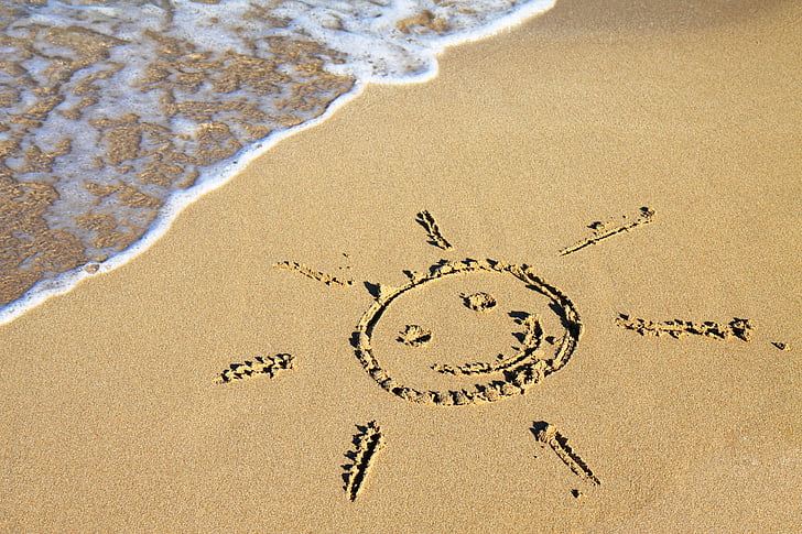 photo of sun illustration on sand near body of water during daytime