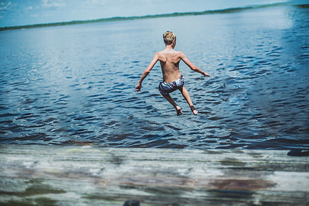 boy jumping towards blue sea