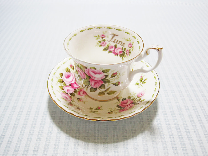 white-pink-and-green floral ceramic cup and saucer on whtie textile