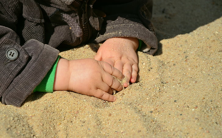 closeup photo of kid wearing black corduroy jacket holding brown sand