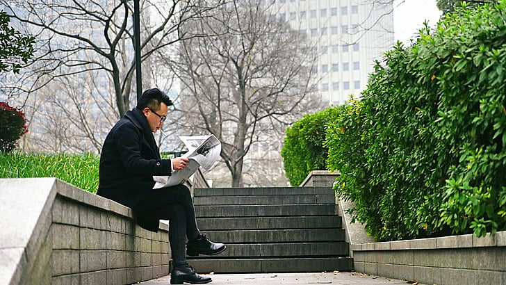 man wearing black coat while reading newspaper