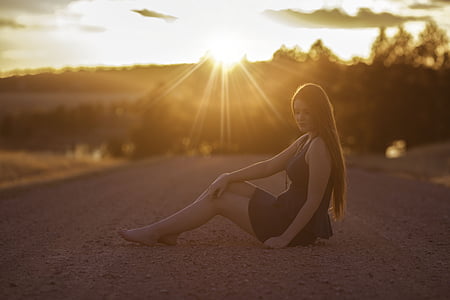 woman wearing black sleeveless dress sitting on road during sunrise