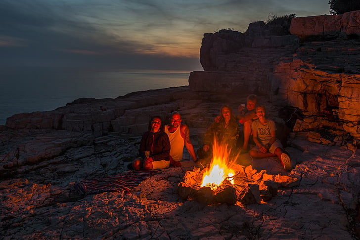 two men and three women sitting on front of campfire
