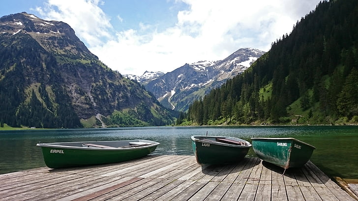 three green canoe boats on brown wooden dock beside body of water near mountains