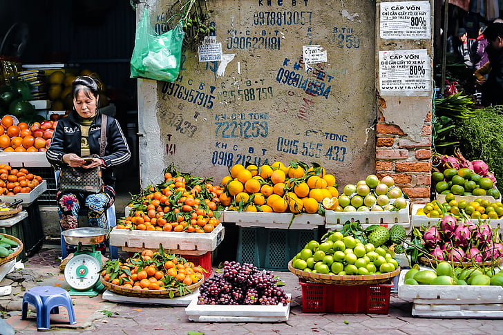 woman wearing black track jacket standing in front of weighing scale and fruit stand at daytime