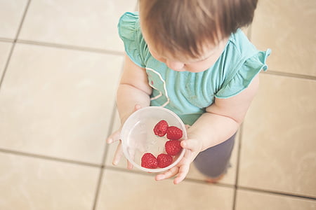 baby holding white bowl filled with raspberries