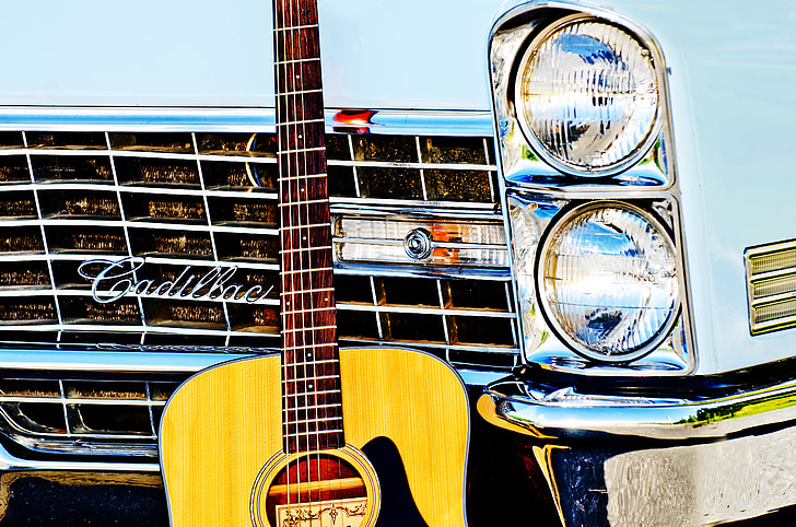 brown acoustic guitar leaning on white Cadillac car