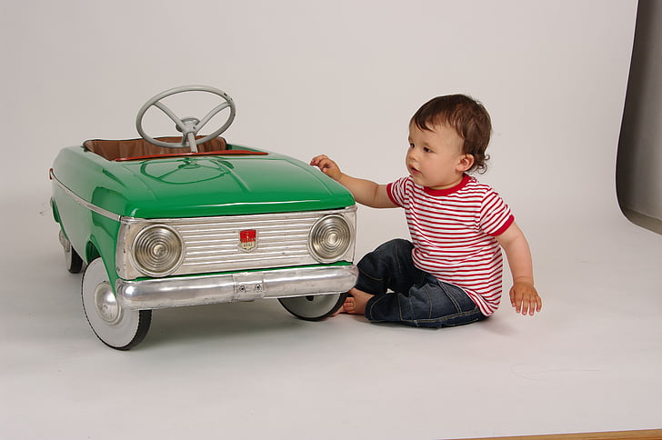 toddler with red and white striped shirt next to teal ride-on vehicle