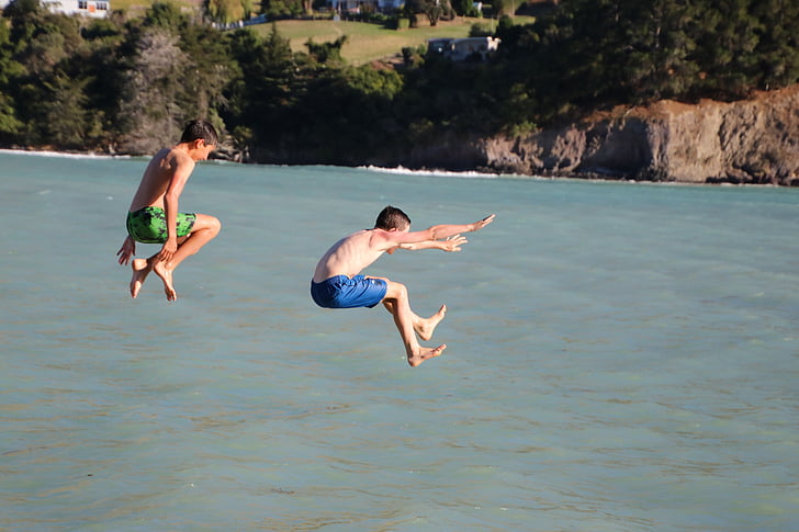 two boys jumping on body of water