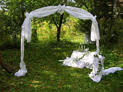 white wedding archway surrounded by green leaf trees