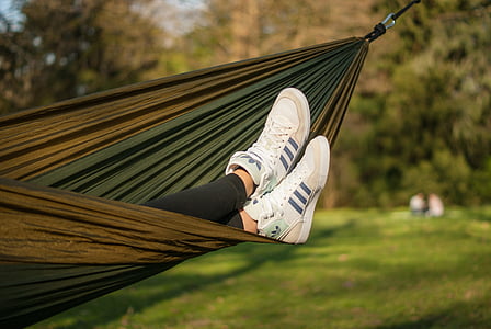 person on hammock wearing white and black Adidas sneakers