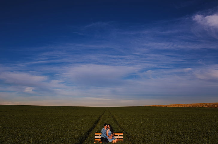 man and woman sitting on bench overlooking green field during daytime