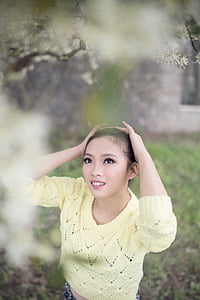 woman in yellow sweater holding her head while looking on flower