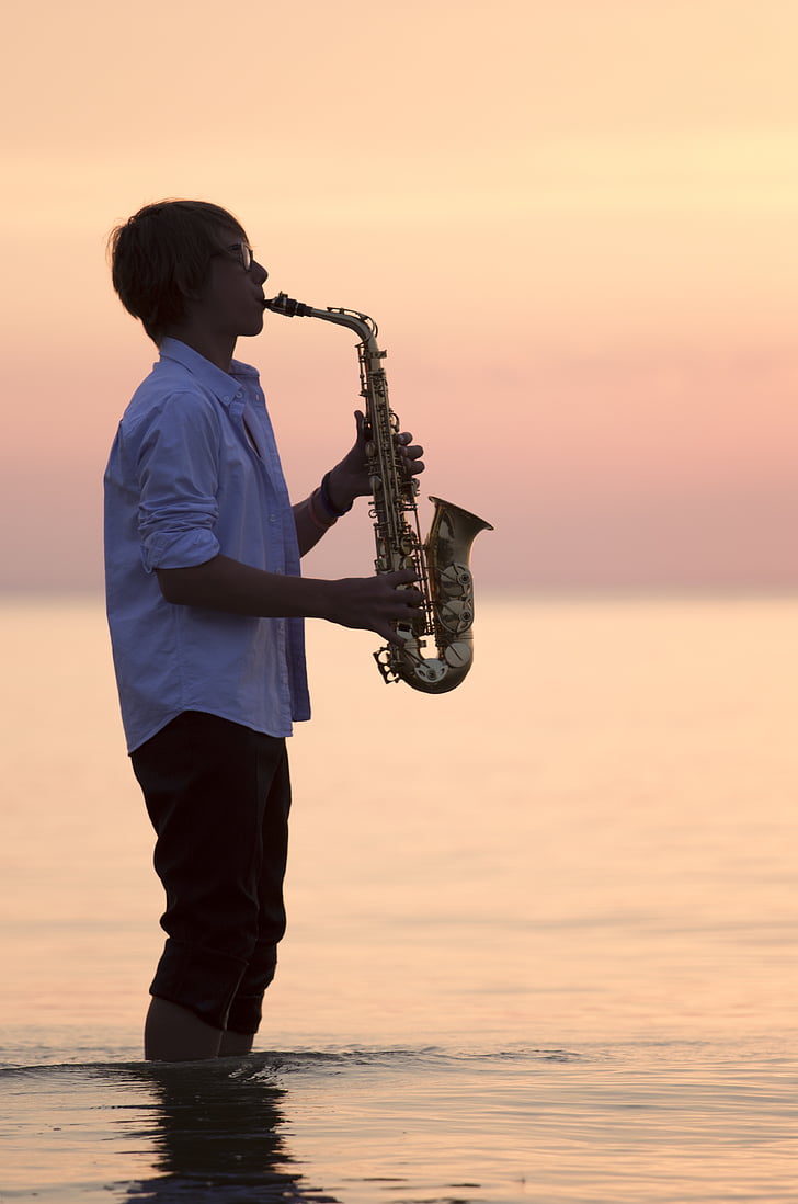 man playing saxophone standing on body of water during golden hour