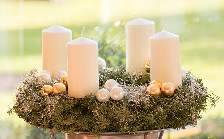 four white pillar candles on top of green wreath