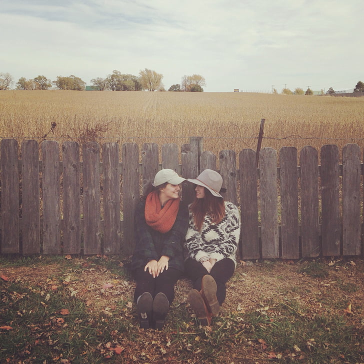 two women leaning on brown wooden fences