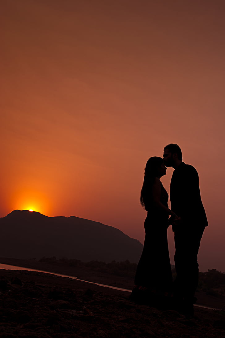 silhouette of man kissing forehead of woman during sunset