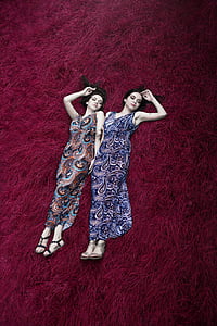 two women wearing multicolored paisley-print dresses lying on red surface