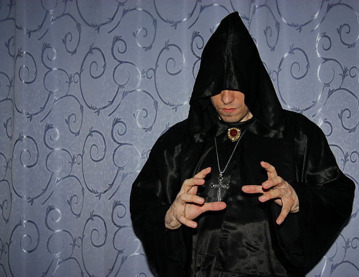 person wearing black robe and silver-colored crucifix necklace using hand gesture