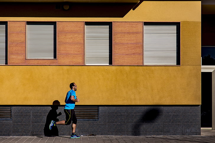 man runs on gray concrete pathway beside yellow building
