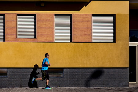 man runs on gray concrete pathway beside yellow building
