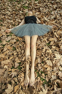 woman wearing black and gray dress lying on ground covered with dried leaves