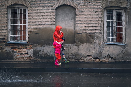 person wearing red rainy coat while with his/her children walking on black asphalt road