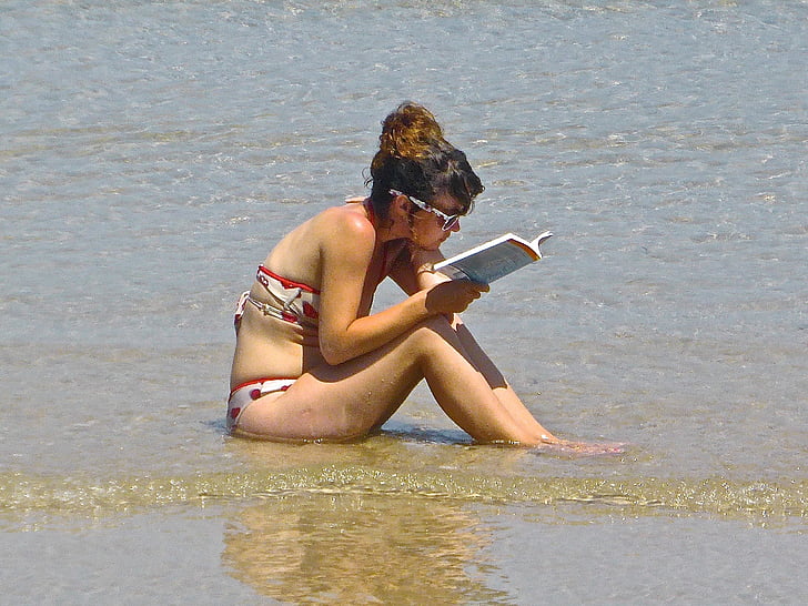 woman wearing white-and-red bikini reading book in seashore