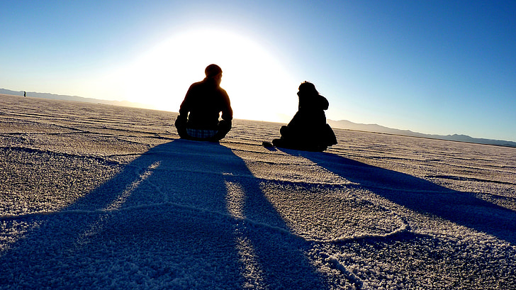man and woman sitting on desert against the sun