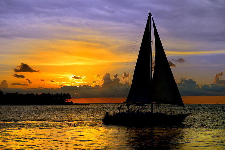 silhouette of sailboat on ocean water during orange sunset
