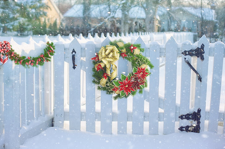 green and red Christmas wreath on white wooden fence
