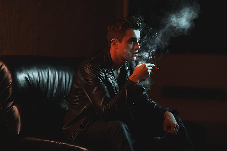 man holding cigarette stick while sitting on chair