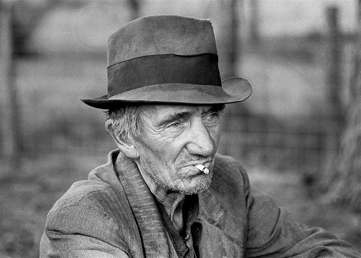 grayscale photo of man with hat and cigarette