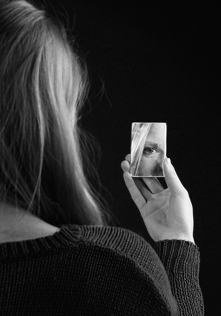 grayscale photography of woman holding piece of mirror