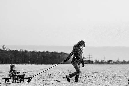 grayscale photography of woman pulling toddler riding sled