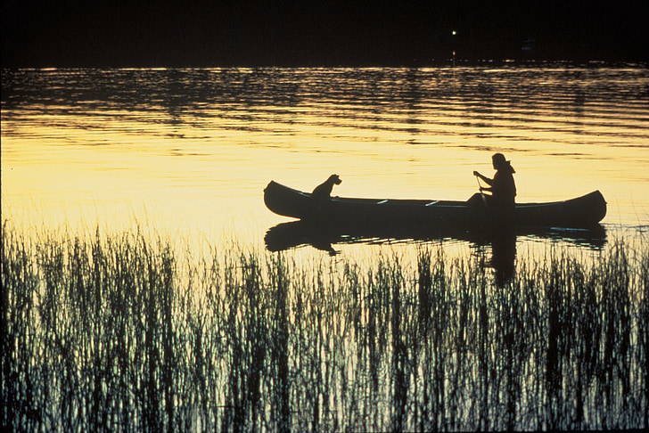silhouette of woman and dog in canoe on body of water