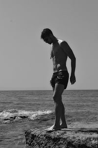 grey scale photography of man in swimming outfit on top of island