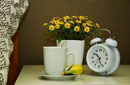 white alarm clock and white ceramic mug on top of white table