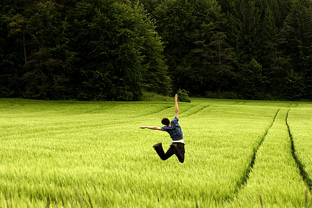 man wears black shirts jumping on green fields near forest during daytime