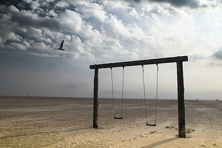black wooden framed two wooden swing on seashore under white clouds
