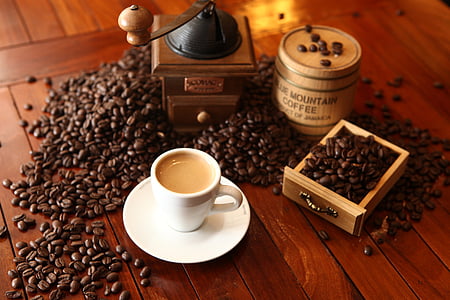 cup of coffee beside coffee beans and coffee grinder
