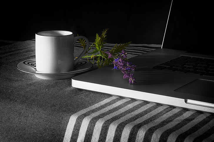 white ceramic mug on saucer beside black laptop